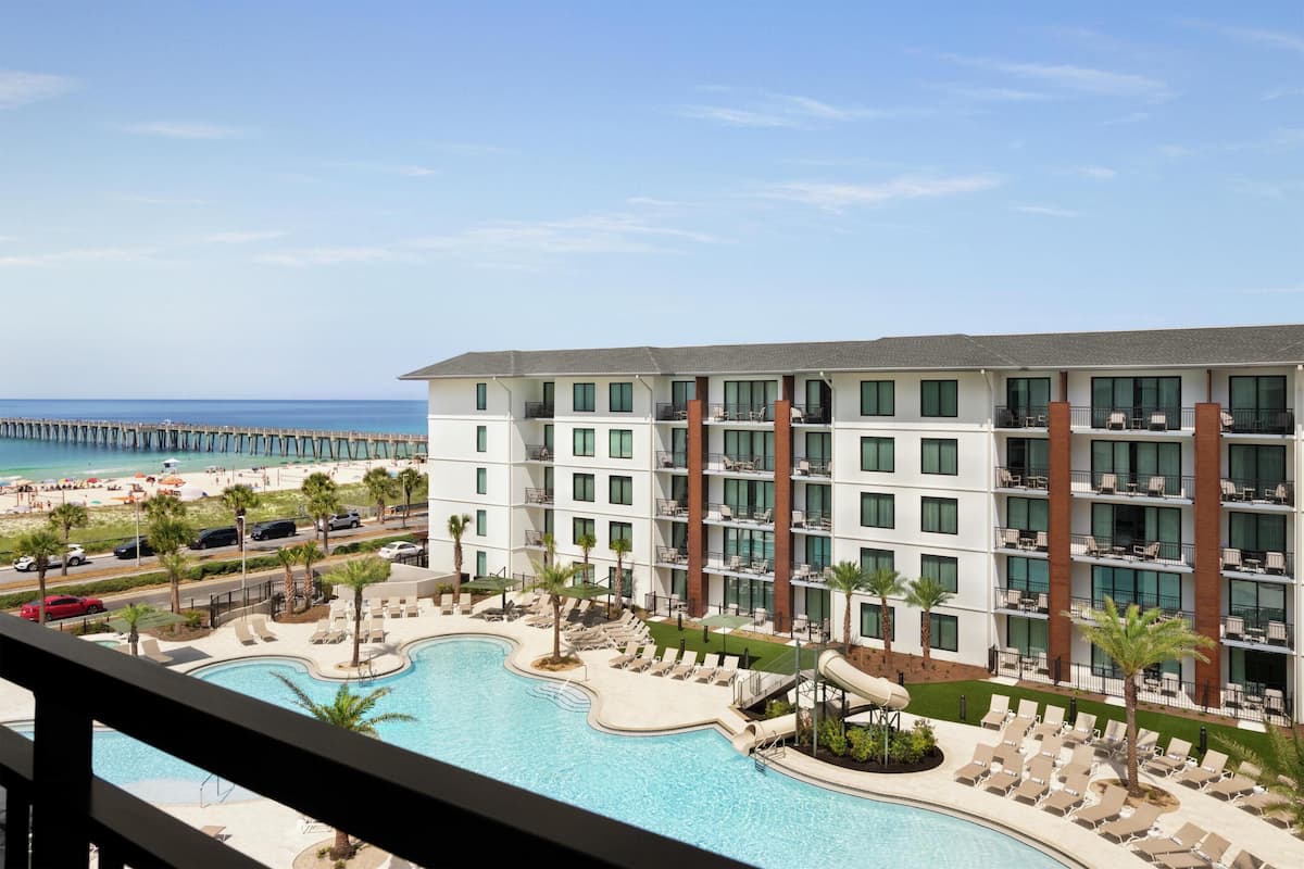 A hotel with a pool, beach view, and a pier in the background.