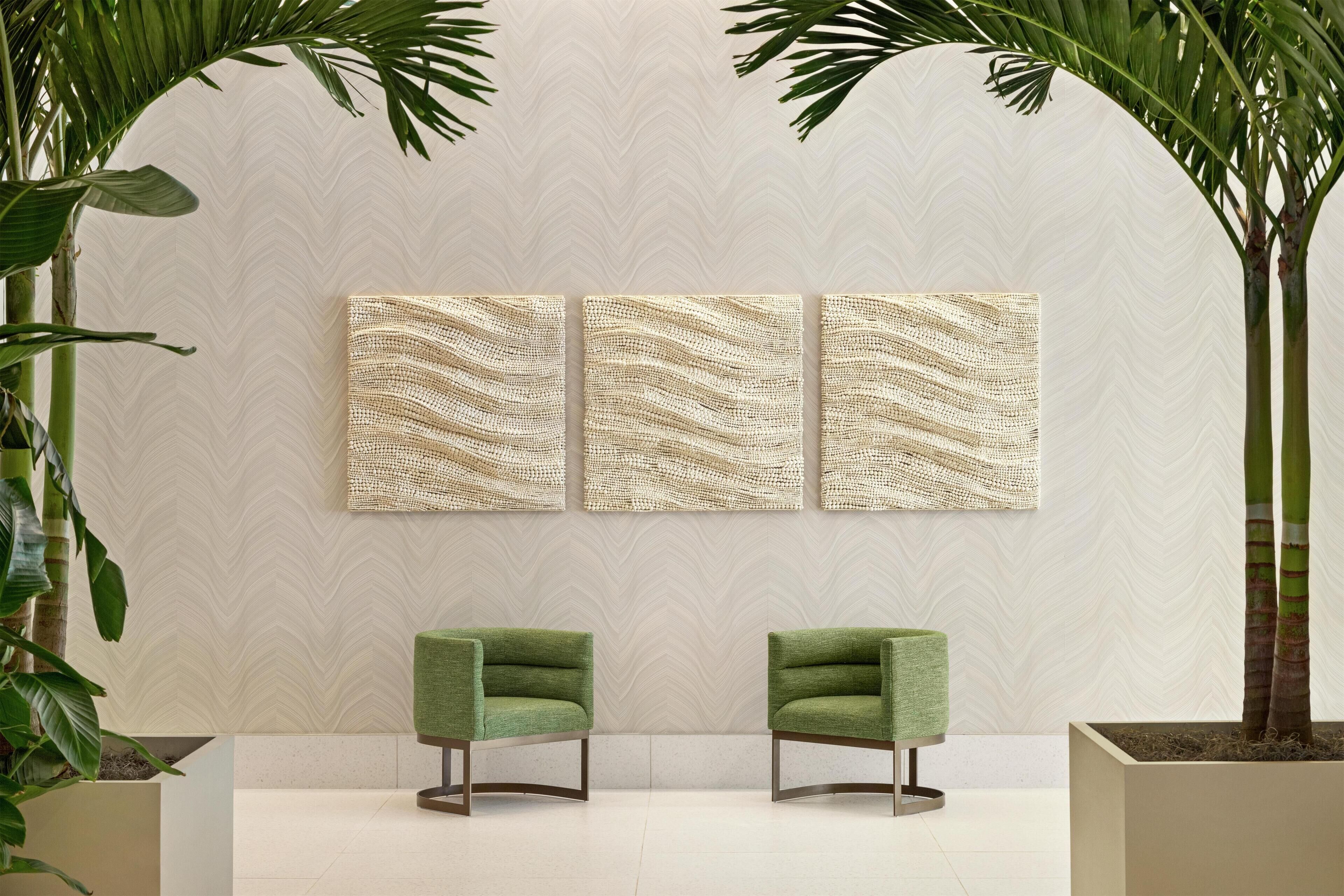 A room with a herringbone-patterned wall, two green armchairs, and a potted plant.
