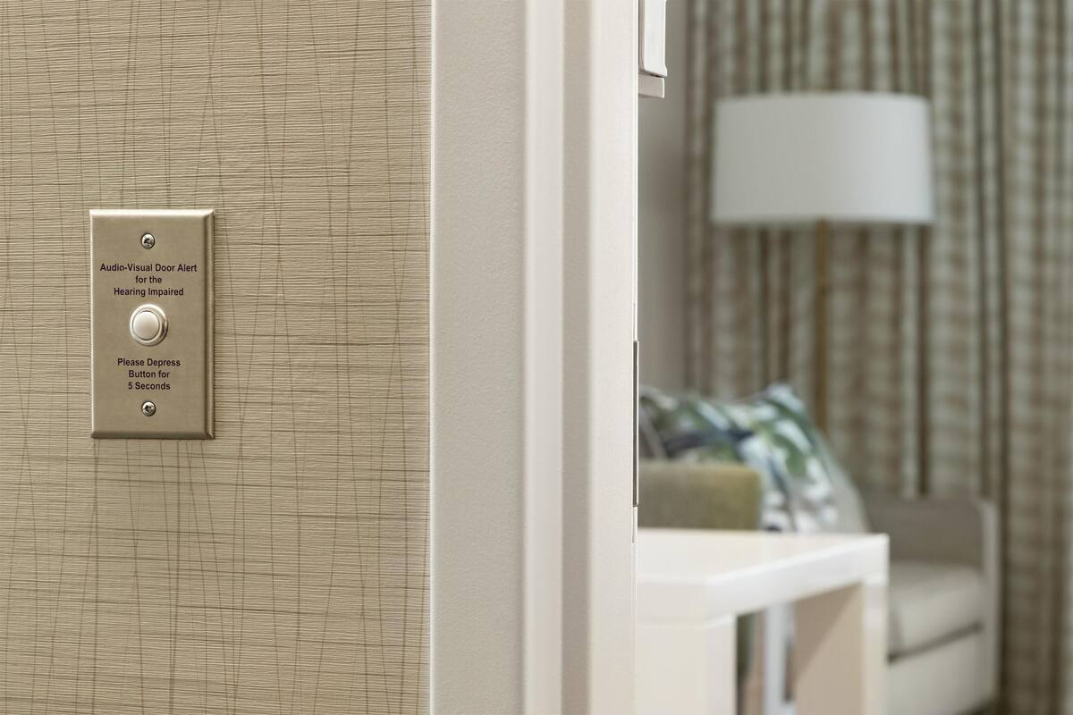 A door with an audio-visual alert system for the hearing impaired, a white wall, and a lamp in the background.