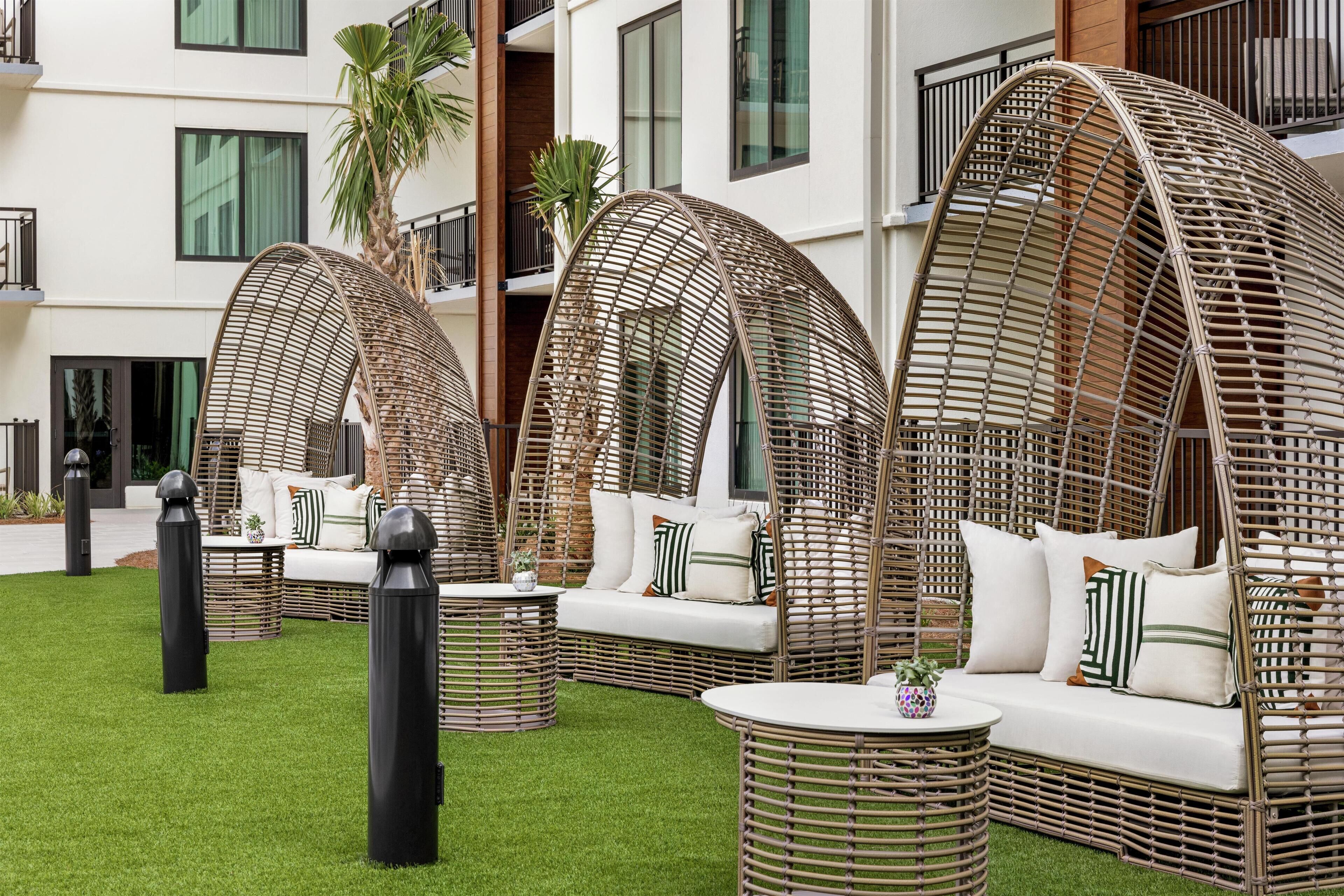 Outdoor wicker furniture with cushions, arranged on a green lawn with a building in the background.