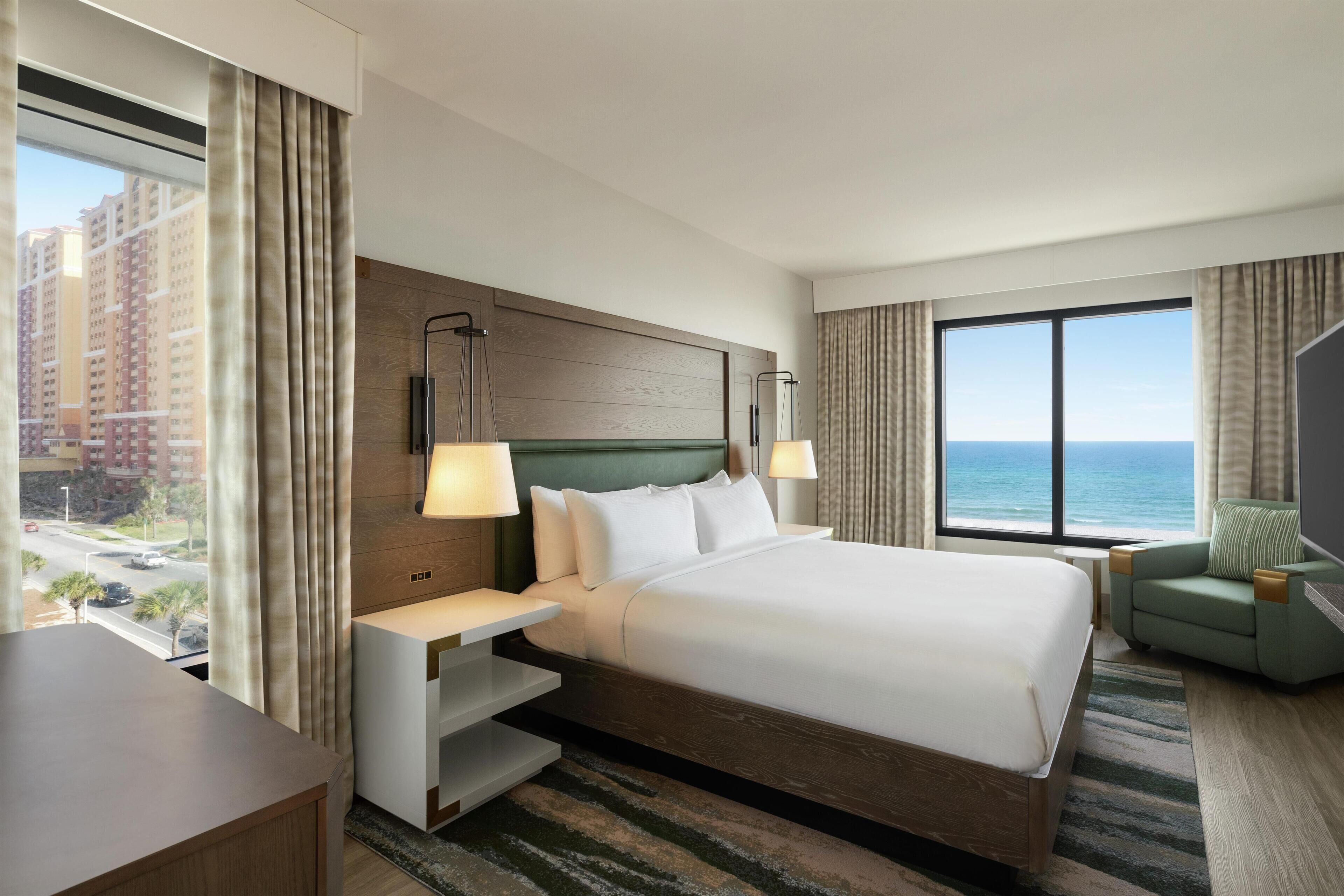 Habitación de hotel con una cama grande, un escritorio, una silla y vistas al océano.