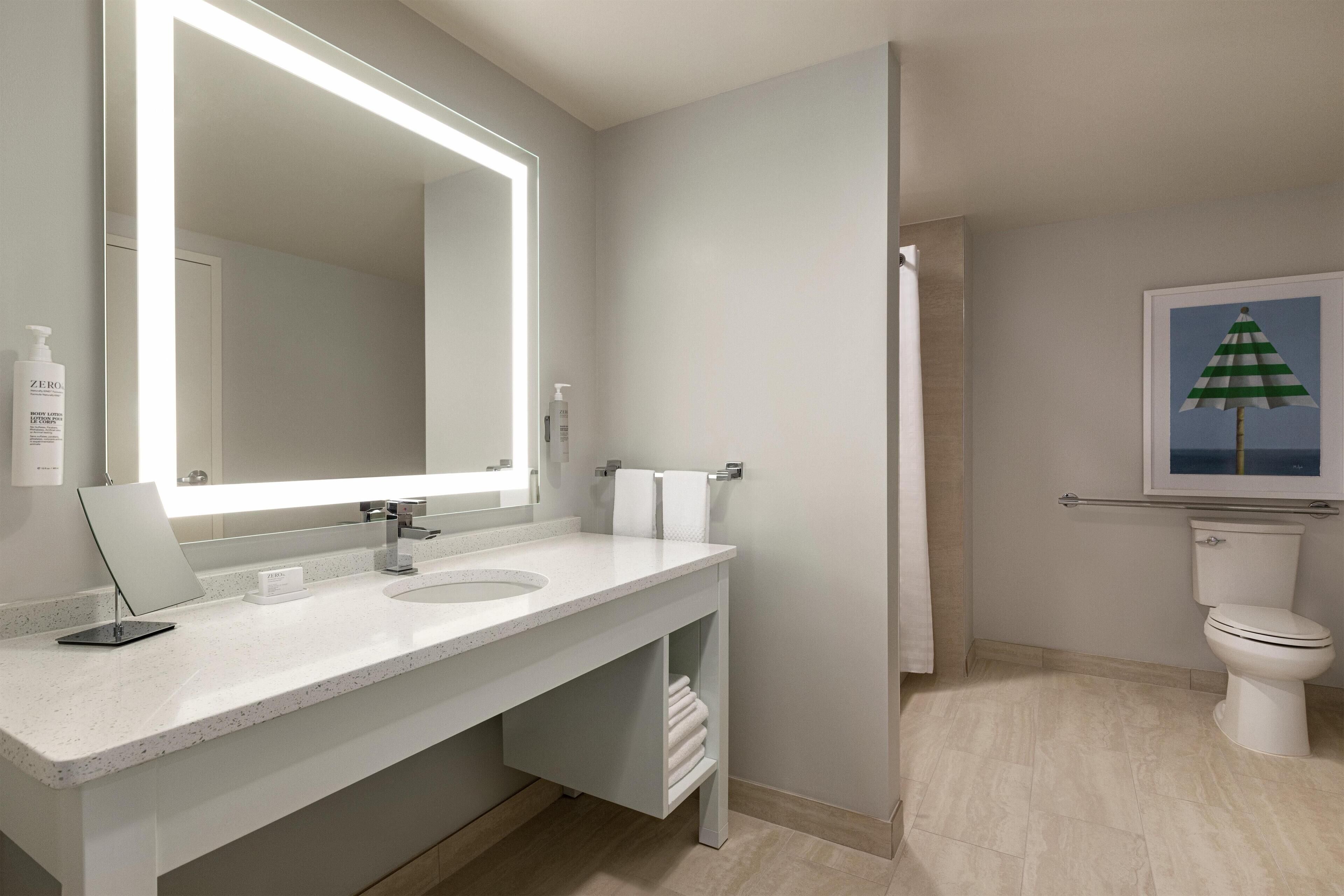 Une salle de bain moderne avec un grand miroir, un lavabo blanc, des toilettes et un porte-serviettes.