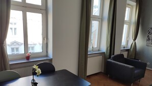 Una habitación con una mesa de comedor, dos sillas, un sofá y dos ventanas con cortinas.