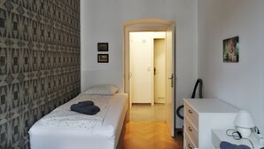 Habitación de hotel con dos camas, un armario, un escritorio con lámpara y cortina estampada.