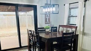 A dining area with a dark wooden table and chairs, a hanging light fixture, and a view through a sliding glass door to an outdoor area. - New Remodel 3BD/2Bath Weekly/Monthly Discounts available (Enid)