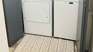 A compact laundry room with a front-loading washer and dryer, wooden cabinets above, and a patterned rug on the floor.