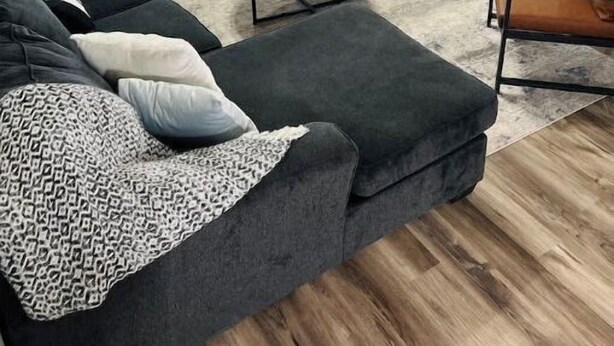 A modern living room with a dark grey sectional sofa, a leather armchair, a small wooden coffee table, a fireplace, and a flat-screen TV mounted on the wall. - New Remodel 3BD/2Bath Weekly/Monthly Discounts available (Enid)