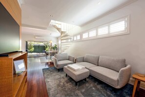 A modern living room with a sectional sofa, ottoman, and a wooden reception desk. - Renovated 3BR Family Home in Richmond with Parking (Richmond)
