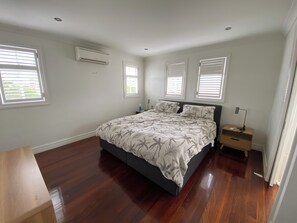 A bedroom with a bed, bedside tables, an air conditioner, and windows with blinds.