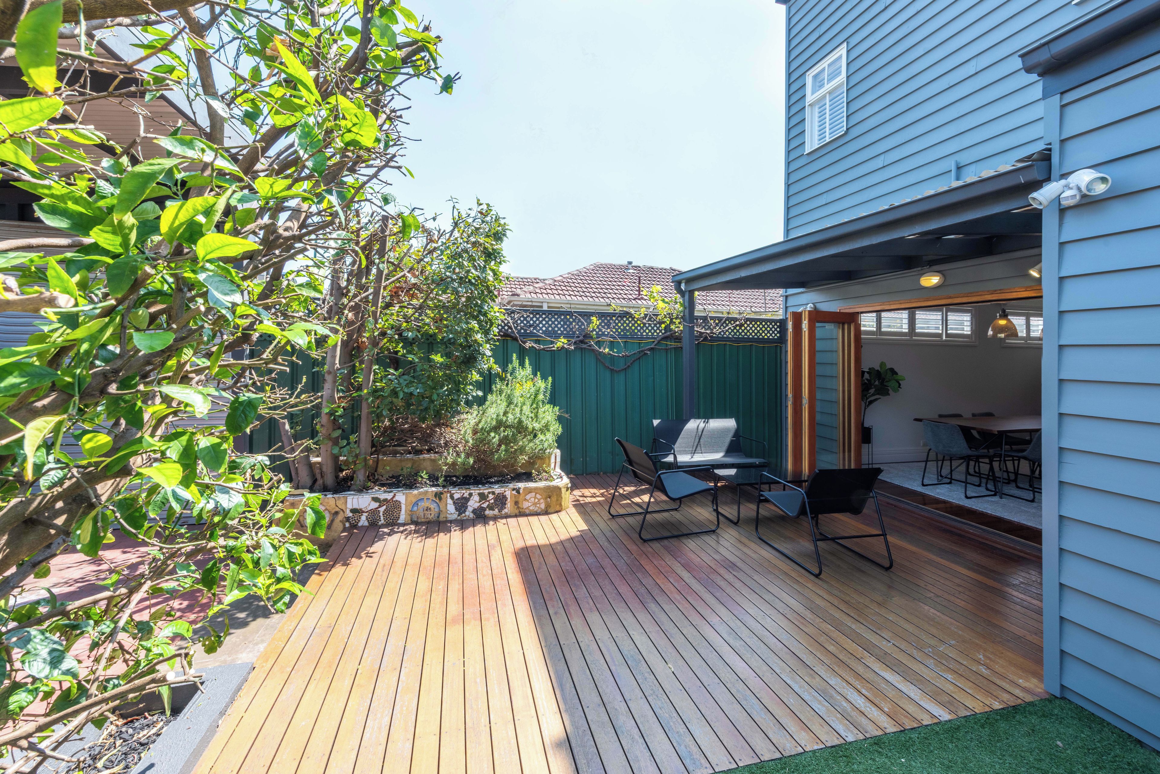A wooden deck with outdoor furniture, a green fence, and a house with a blue exterior.