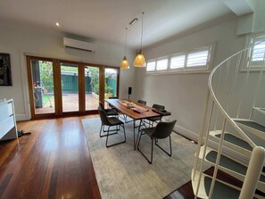 A spacious room with a wooden dining table, chairs, a staircase, and a view through a glass door to an outdoor area. - Renovated 3BR Family Home in Richmond with Parking (Richmond)