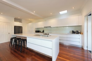 Cocina moderna con armarios blancos, refrigerador de acero inoxidable, una isla grande con lavamanos y piso de madera.