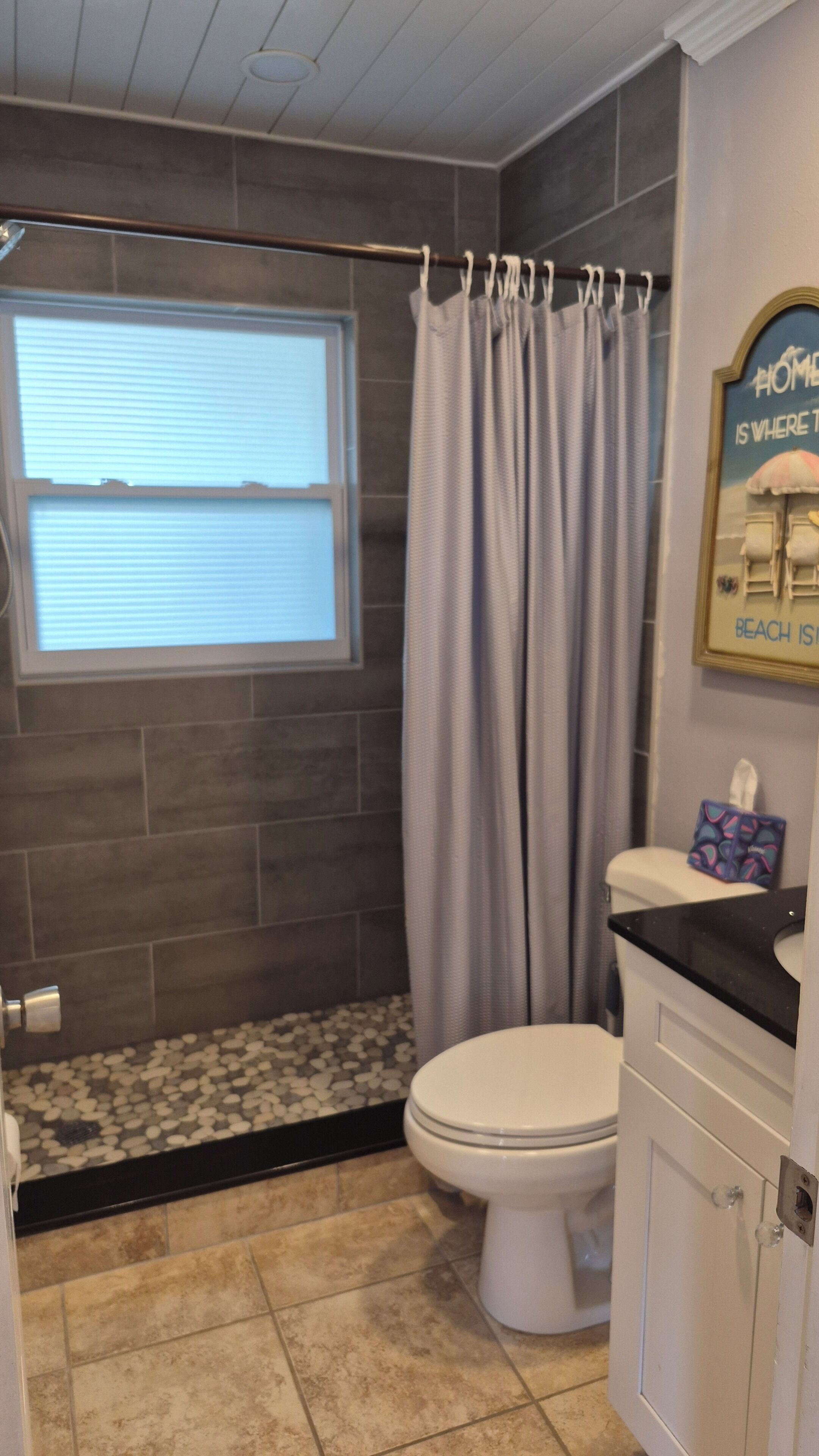 Een badkamer met een douche, toilet en een raam met zonwering.