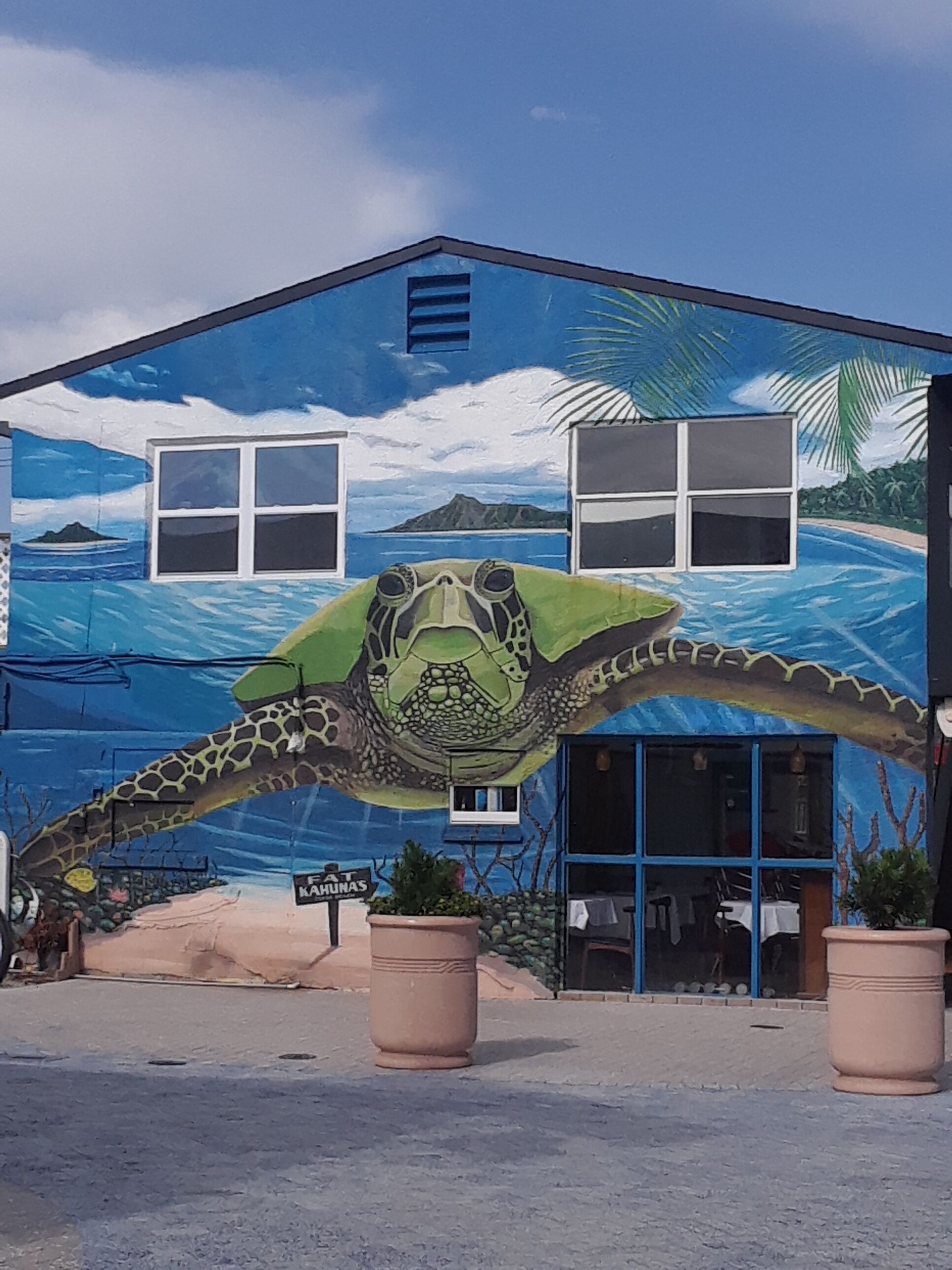 Un edificio con un mural de una tortuga marina y una escena de playa tropical.