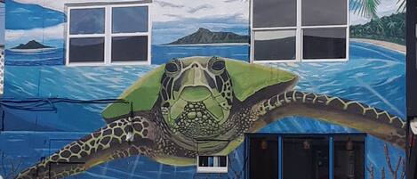 Un edificio con un mural de una tortuga marina y una escena de playa tropical.