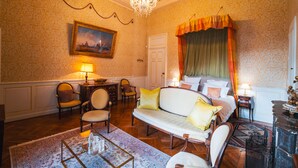 A room with a bed, a sofa, two chairs, a table with a lamp, a painting on the wall, and a chandelier. - Château de Thorens (Fillière)