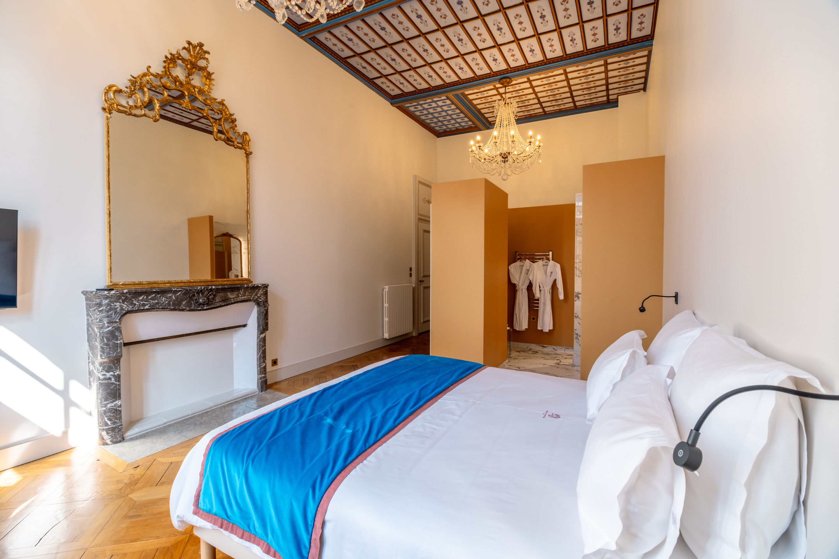 Une chambre à coucher avec un grand lit, une cheminée en marbre, un lustre et un plafond orné de motifs floraux.