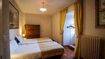 A hotel room with two beds, a wooden dresser, a radiator, and a window with yellow curtains.