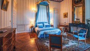 A bedroom with a four-poster bed, a sitting area with a chair and table, and a fireplace. - Château de Thorens (Fillière)