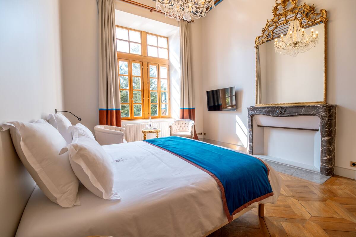 A bedroom with a bed, a television, a fireplace, and a large window.