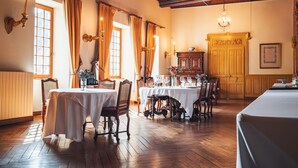 A dining room with wooden floors, white tablecloths, and a chandelier. - Château de Thorens (Fillière)
