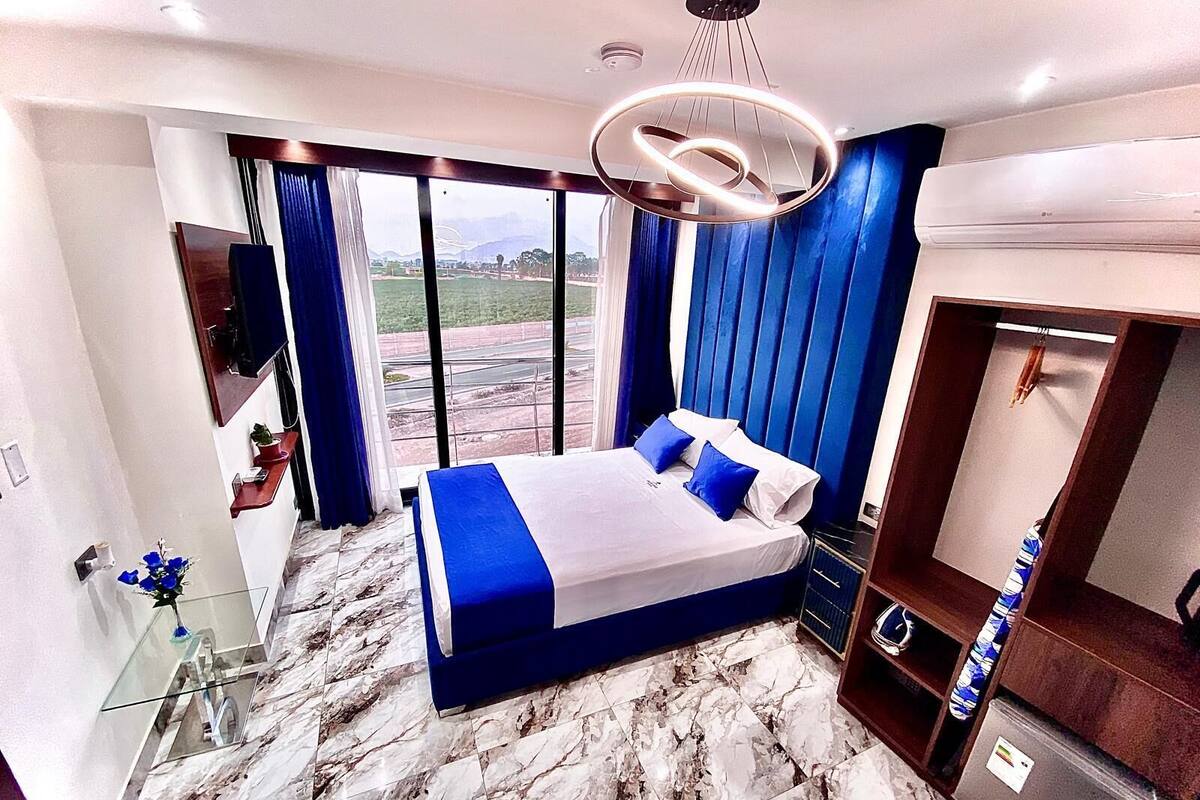 A modern hotel room with a large bed, a wardrobe, a vanity with a mirror, and a view of the outdoors.