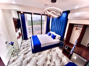 A modern hotel room with a large bed, a wardrobe, a vanity with a mirror, and a view of the outdoors.