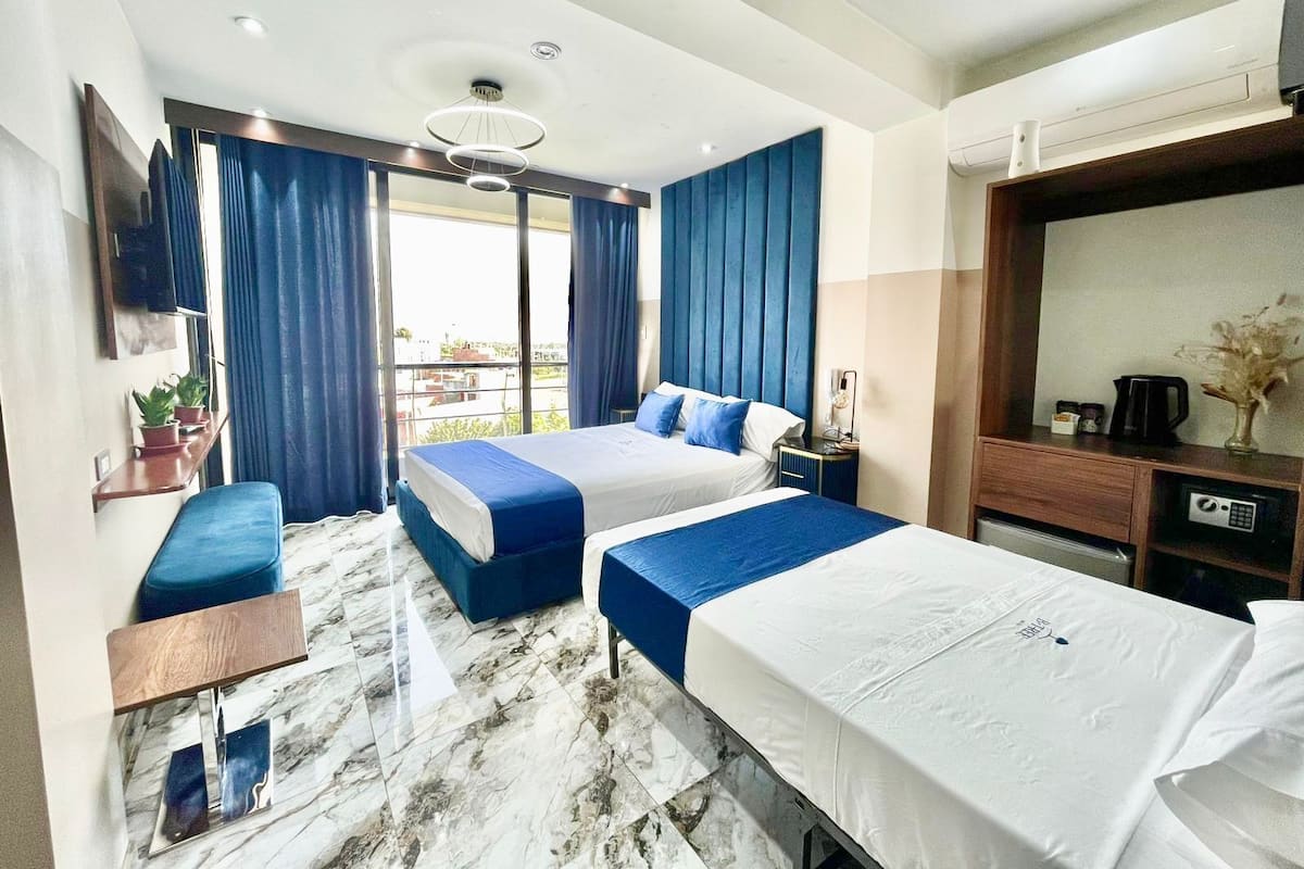 A hotel room with two beds, a desk, a chair, a TV, a coffee maker, and a view of the city.