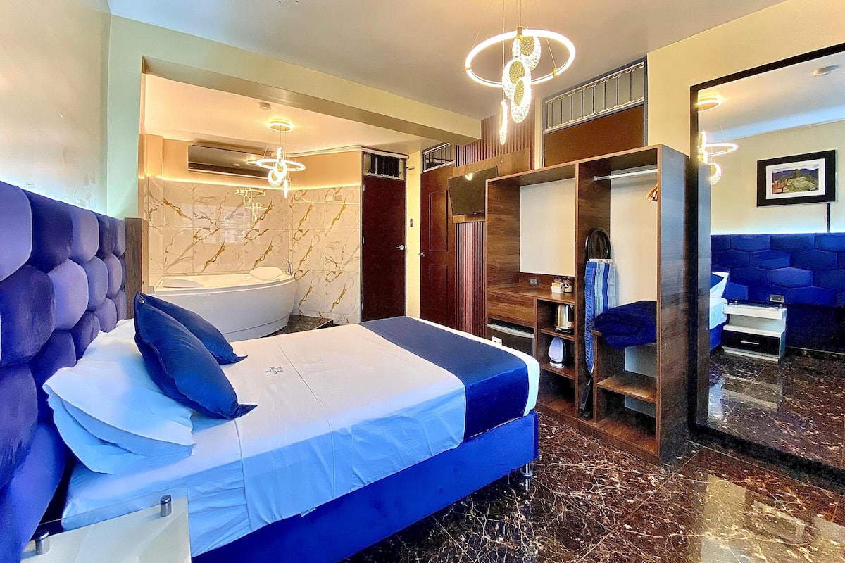A modern hotel room with a large bed, a separate bathroom with a bathtub, a walk-in closet, and a view of the city.
