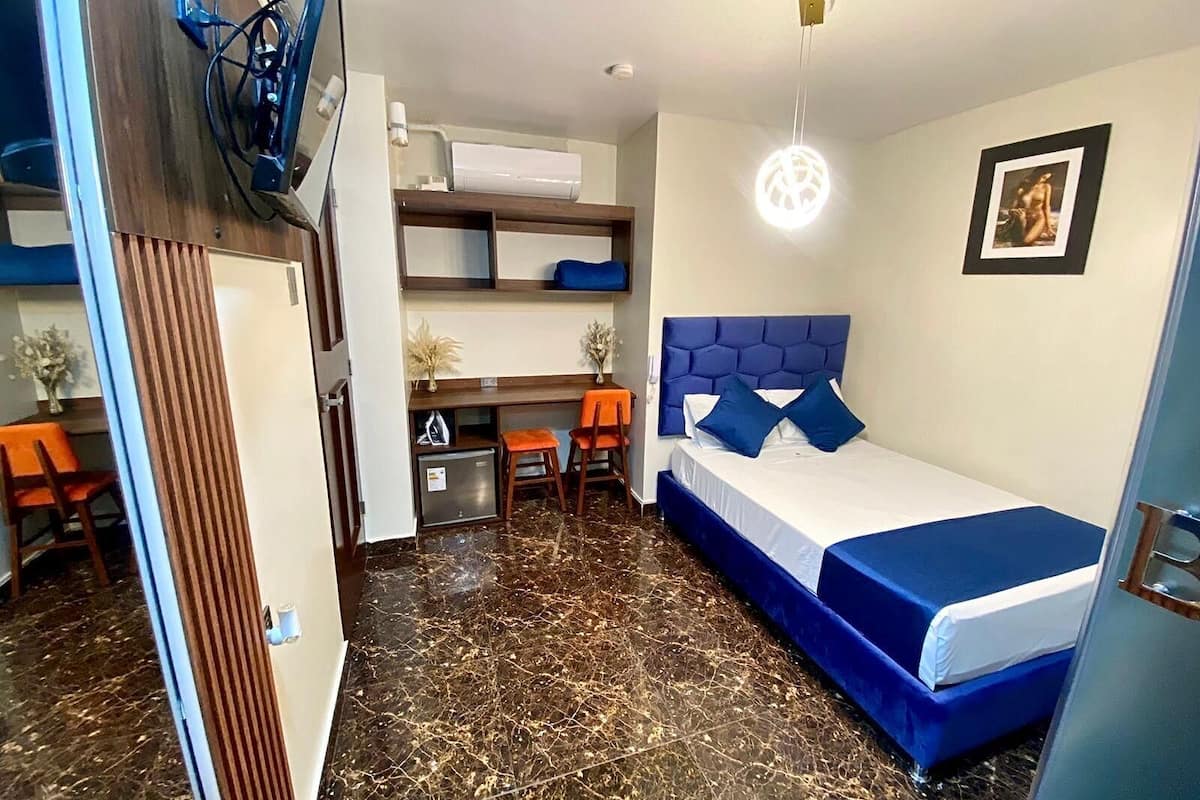 A compact hotel room with a bed, a desk, and a small kitchenette.