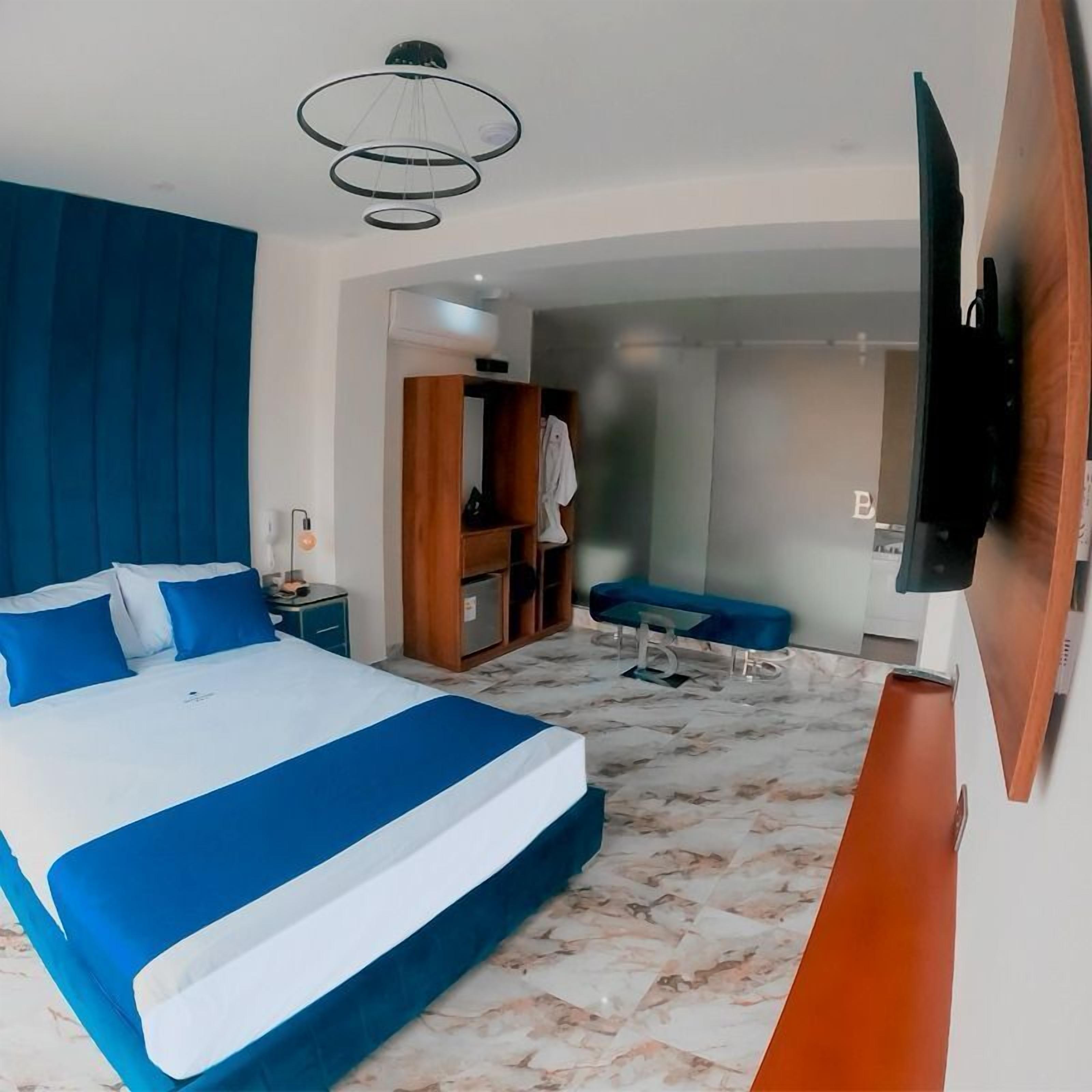 A modern hotel room with a large bed, a desk, a chair, a TV mounted on the wall, and a bathroom visible through an open door.
