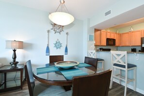 A dining area with a round table, chairs, a bowl, placemats, a lamp, and nautical-themed wall decorations. - 6th Floor condo at The Palms of Destin with Seasonal Beach Shuttle! (Destin)