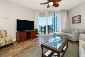 A living room with a flat-screen TV, a glass coffee table, a sofa, a patterned armchair, and a balcony with a view. - 6th Floor condo at The Palms of Destin with Seasonal Beach Shuttle! (Destin)