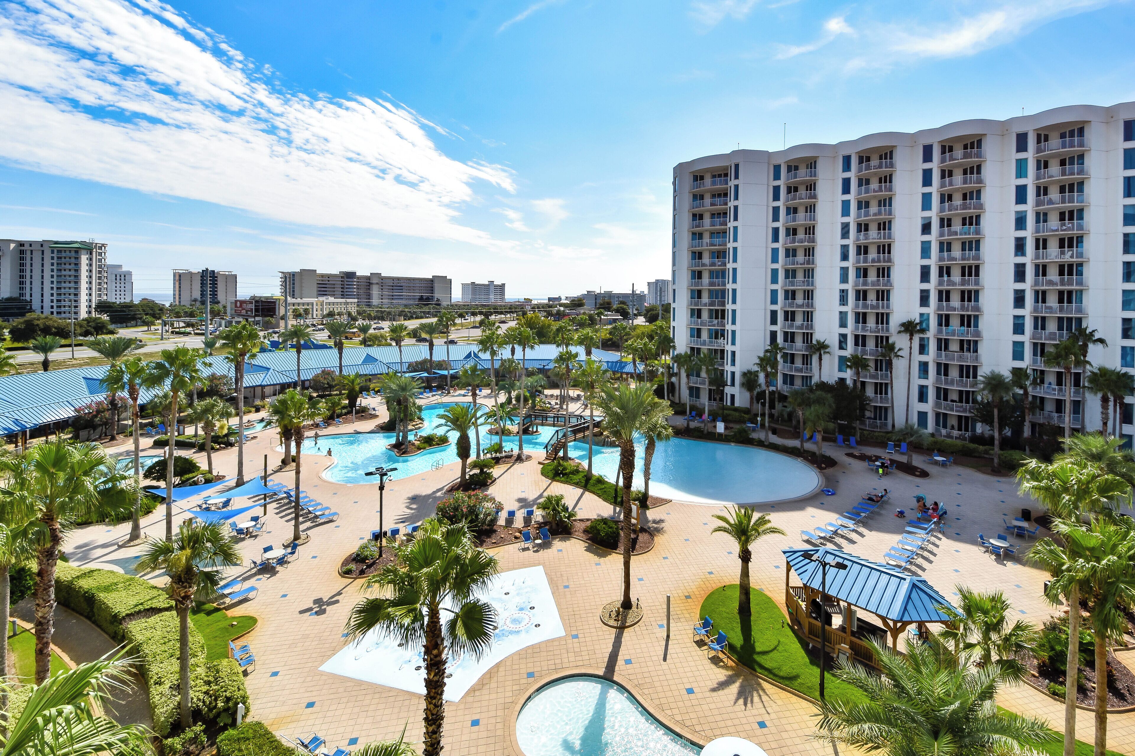 A resort with multiple swimming pools, palm trees, and a large building with balconies.