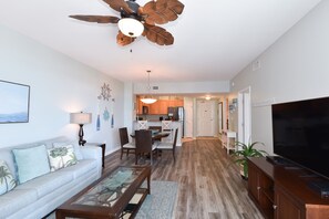 A modern living room with a sofa, coffee table, TV, and a ceiling fan. - 6th Floor condo at The Palms of Destin with Seasonal Beach Shuttle! (Destin)