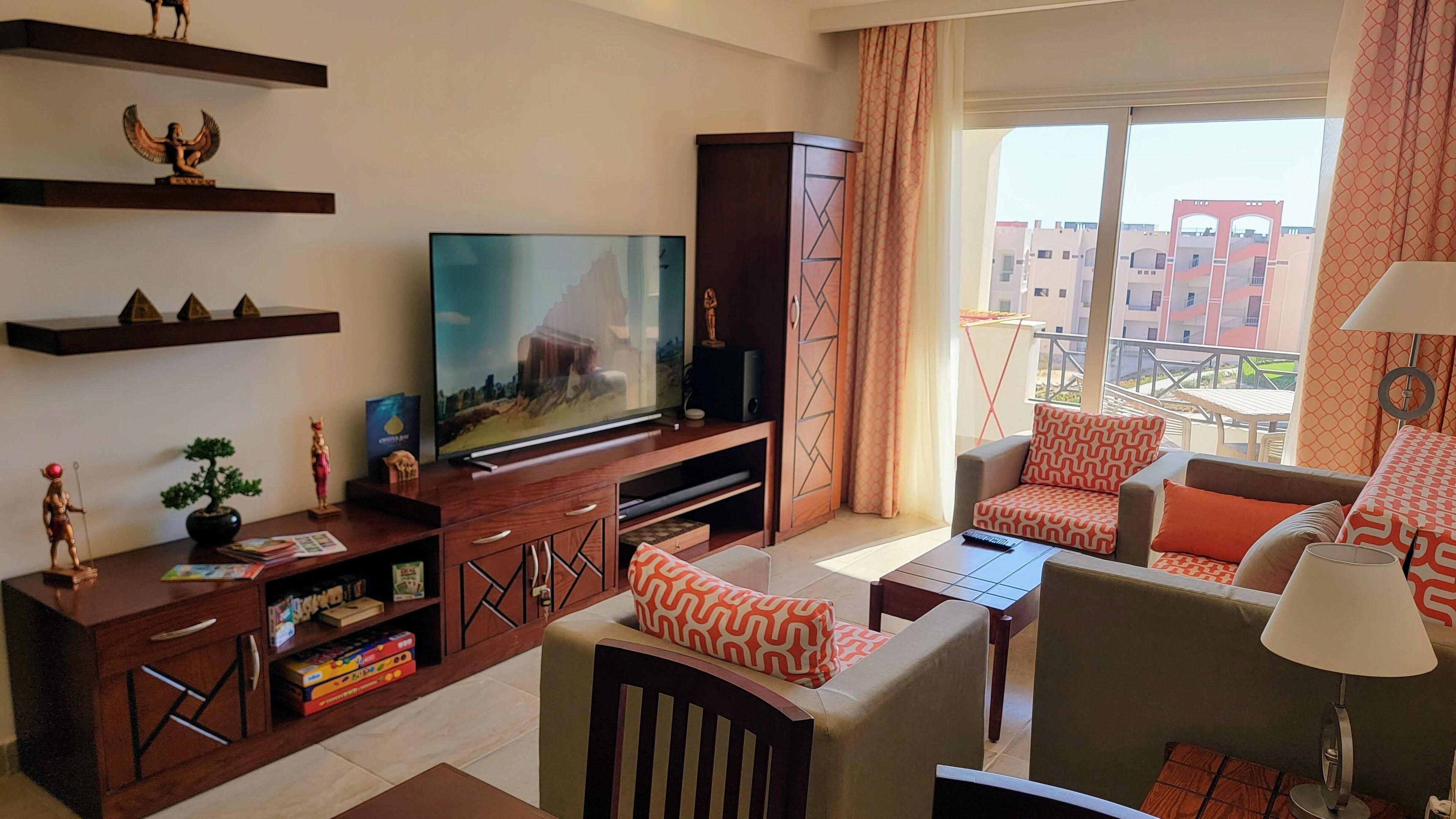 A modern living room with a flat-screen TV, wooden entertainment unit, and a sofa with patterned cushions.