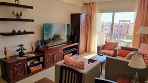 Una sala de estar moderna con televisor de pantalla plana, mueble de entretenimiento de madera y un sofá con cojines estampados.