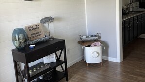A living room with a wooden floor, a black console table with decorative items, a large wall clock, and a kitchen visible through an open doorway. - Pigs Ina Blanket - Minutes from Rend Lake and I-64/I-57 (Ina)