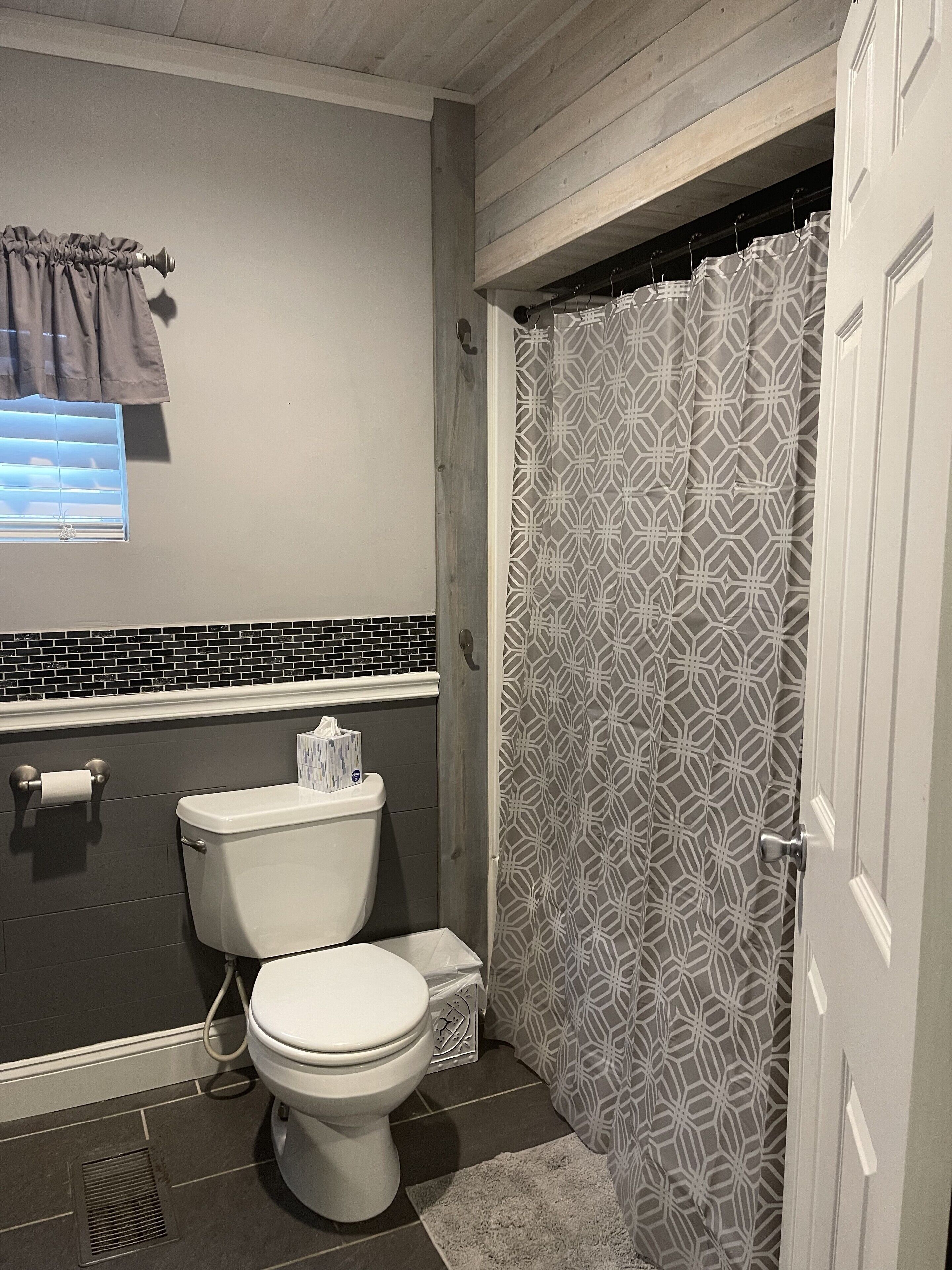 Un baño con inodoro, cortina de ducha y ventana con persianas.
