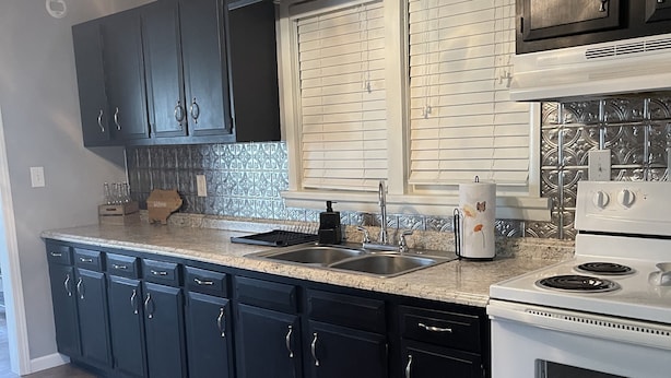 A kitchen with dark cabinets, a white stove, a window with blinds, and a ceiling fan. - Pigs Ina Blanket - Minutes from Rend Lake and I-64/I-57 (Ina)