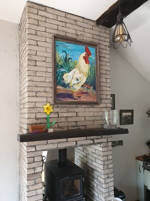 A brick fireplace with a painting of a rooster, a vase with a yellow flower, and a glass vase on the mantel. - Clew Bay Escape - 25% 2 Week Discount, 50% Monthly Discount (Newport)
