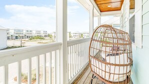 A balcony with a wooden ceiling, white railings, and a wicker birdcage with a cushion.