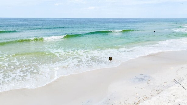 A beach with clear water, a sandy shore, and a distant airplane.