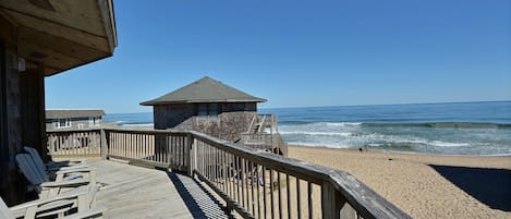 A wooden deck with chairs, a lifeguard tower, and a beach view.