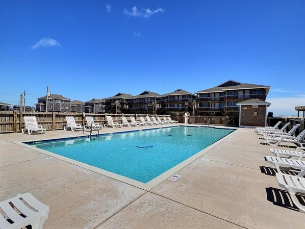 A rectangular swimming pool with lounge chairs and a wooden fence.