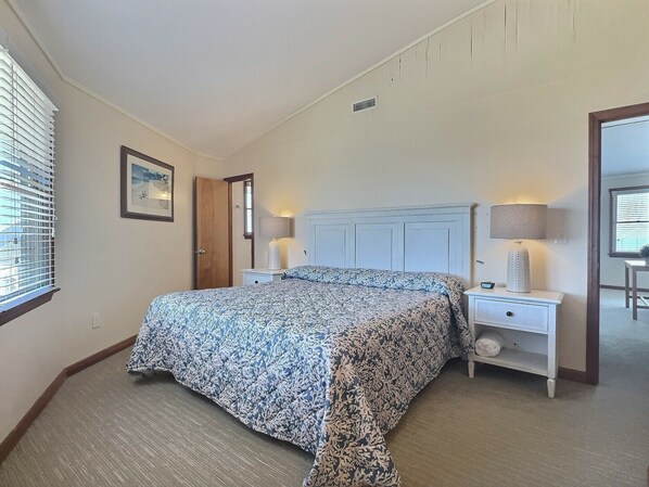 A bedroom with a bed, two bedside tables, a nightstand, a mirror, and a window with blinds.