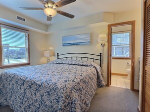 Ein Schlafzimmer mit einem Bett, Deckenventilator, Fenstern und einem Gemälde.