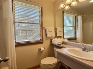 Ein Badezimmer mit Toilette, Waschbecken, Spiegel, Handtuchhalter und einem Fenster mit Jalousien.
