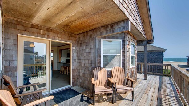 A wooden deck with two Adirondack chairs, a glass door entrance, and a view of the ocean. - Island Fantasea- Short Walk to Beach- Upper and Lower Level (Buxton)