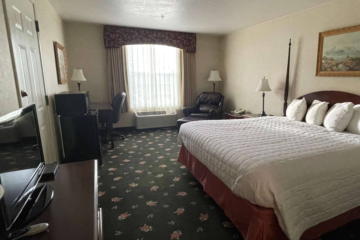 Une chambre d’hôtel avec un grand lit, un bureau avec un ordinateur, une chaise, une fenêtre avec des rideaux et un tableau au mur.